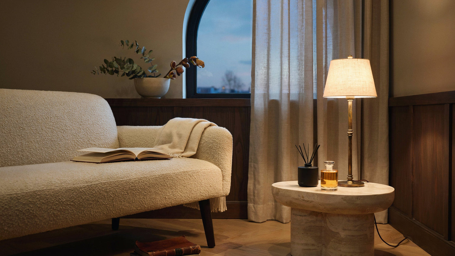 Warm hotel-inspired lounge with home-fragrance details beside a lamp.