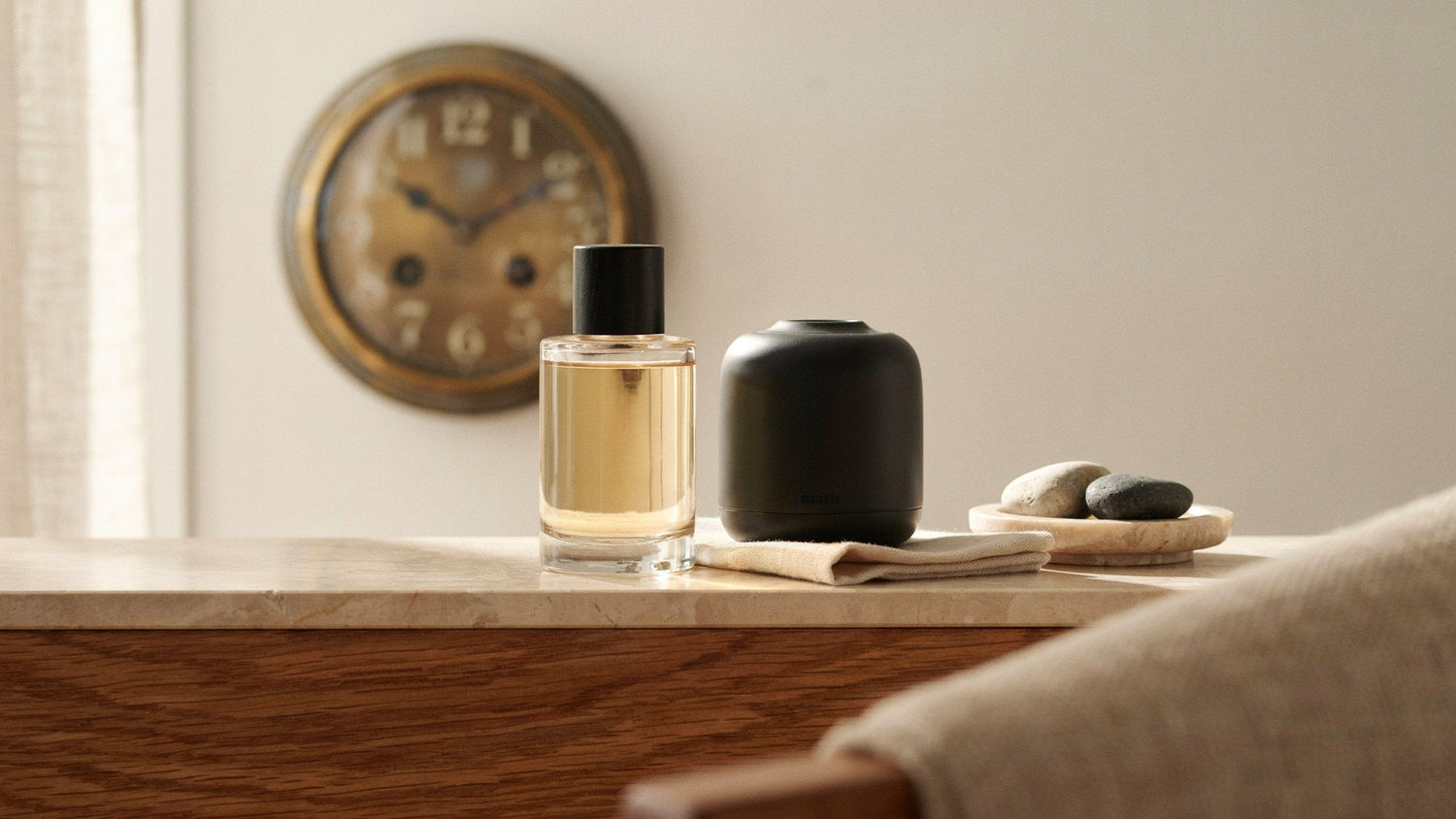 Fragrance oil and waterless diffuser beside a softly blurred clock in a warm living room.